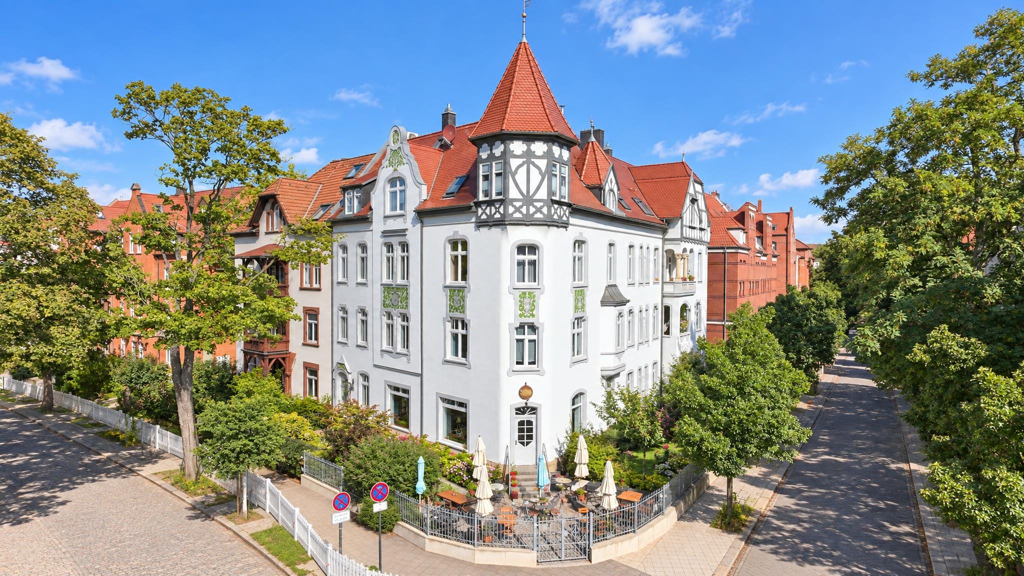 Stadtvilla mit Eckturm und Fachwerkgiebel aus der Luft, davor Terrasse und Baumallee