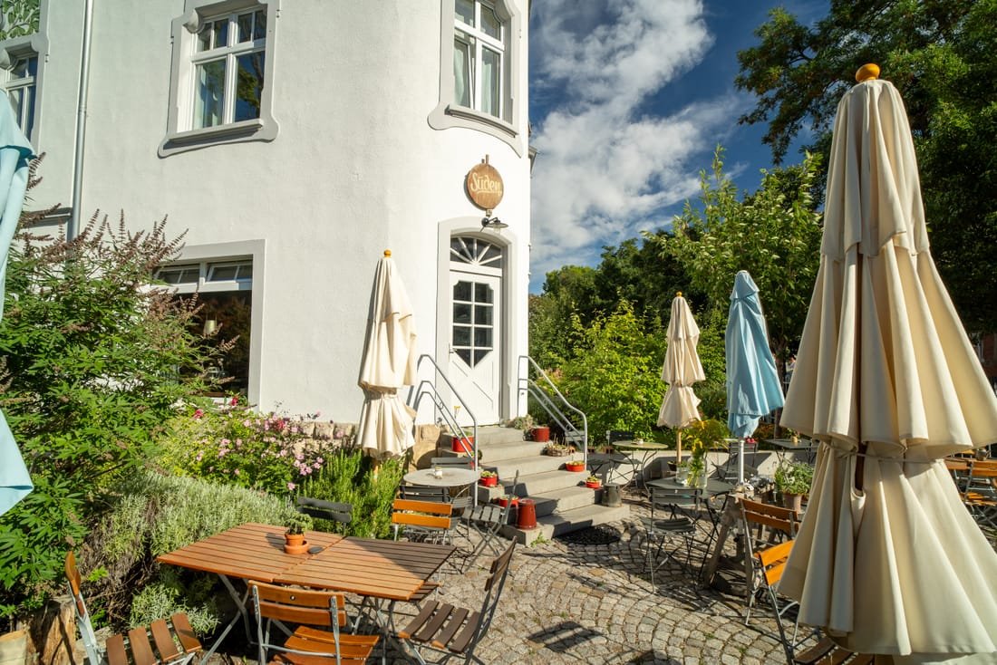 Terrasse mit Tischen und Sonnenschirmen vor dem Eingang der Villa